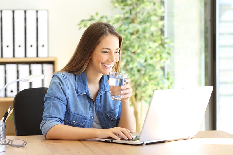 Frau sitzt mit glas Wasser vor Laptop