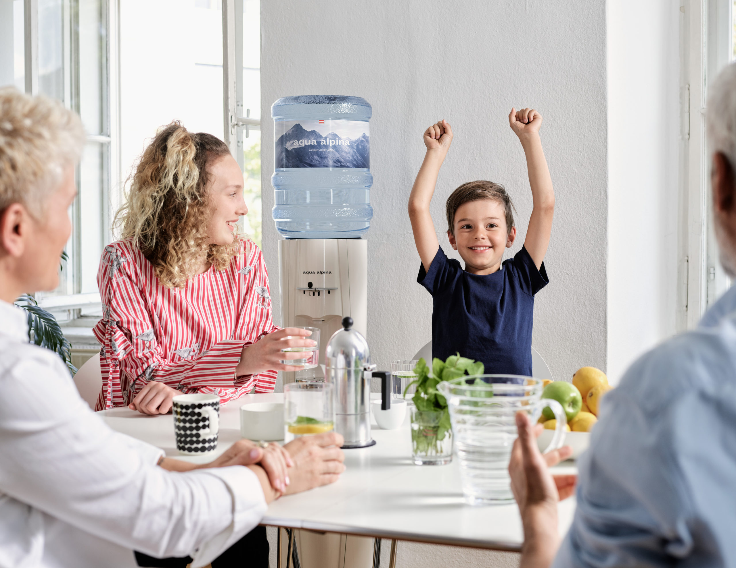 Kind Mit Familie Neben Wasserspender Nimmt Arme In Luft Kind Mit Familie Neben Wasserspender Nimmt Arme In Luft